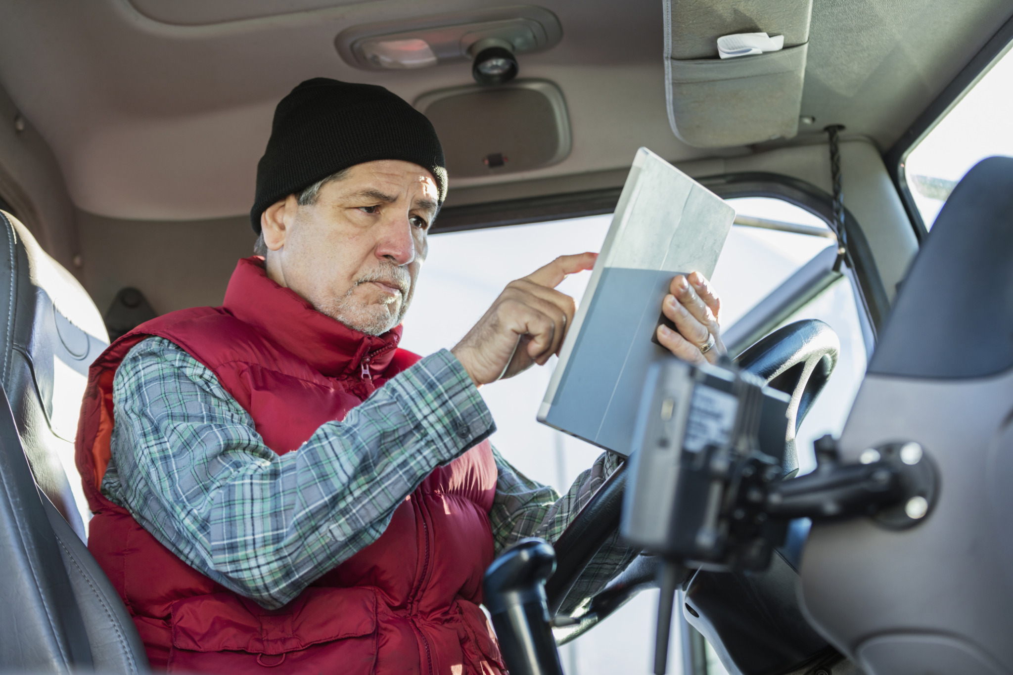 Senior Hispanic man driving semitruck, using tablet Truck & Bus News